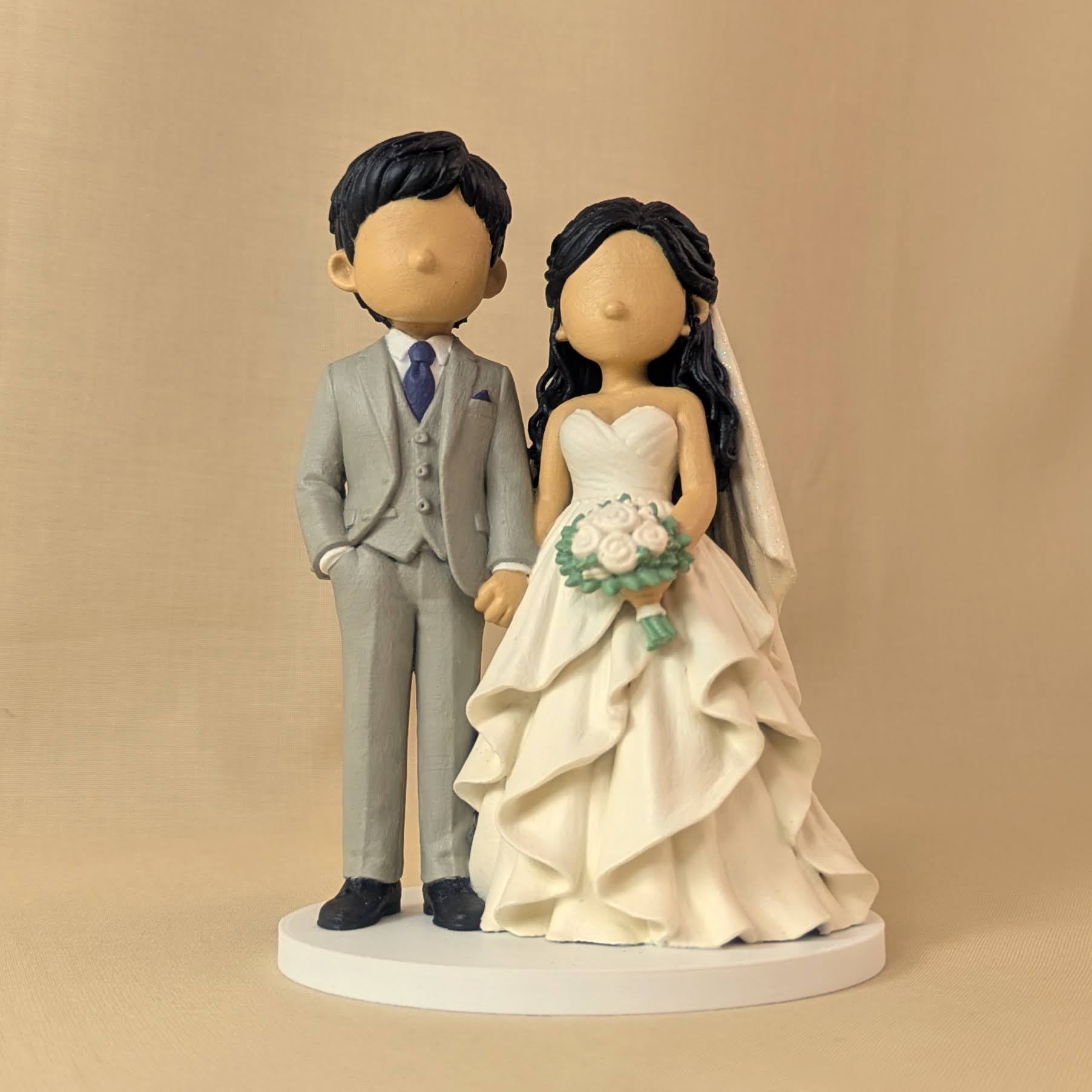 Custom wedding cake topper of a bride and groom holding hands, groom in a grey three-piece suit