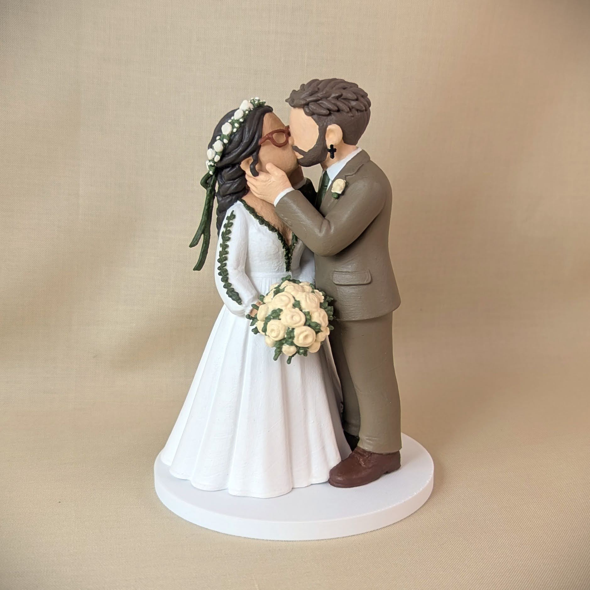 Custom wedding cake topper of a couple kissing, bride in a flower crown and groom in a sage green suit