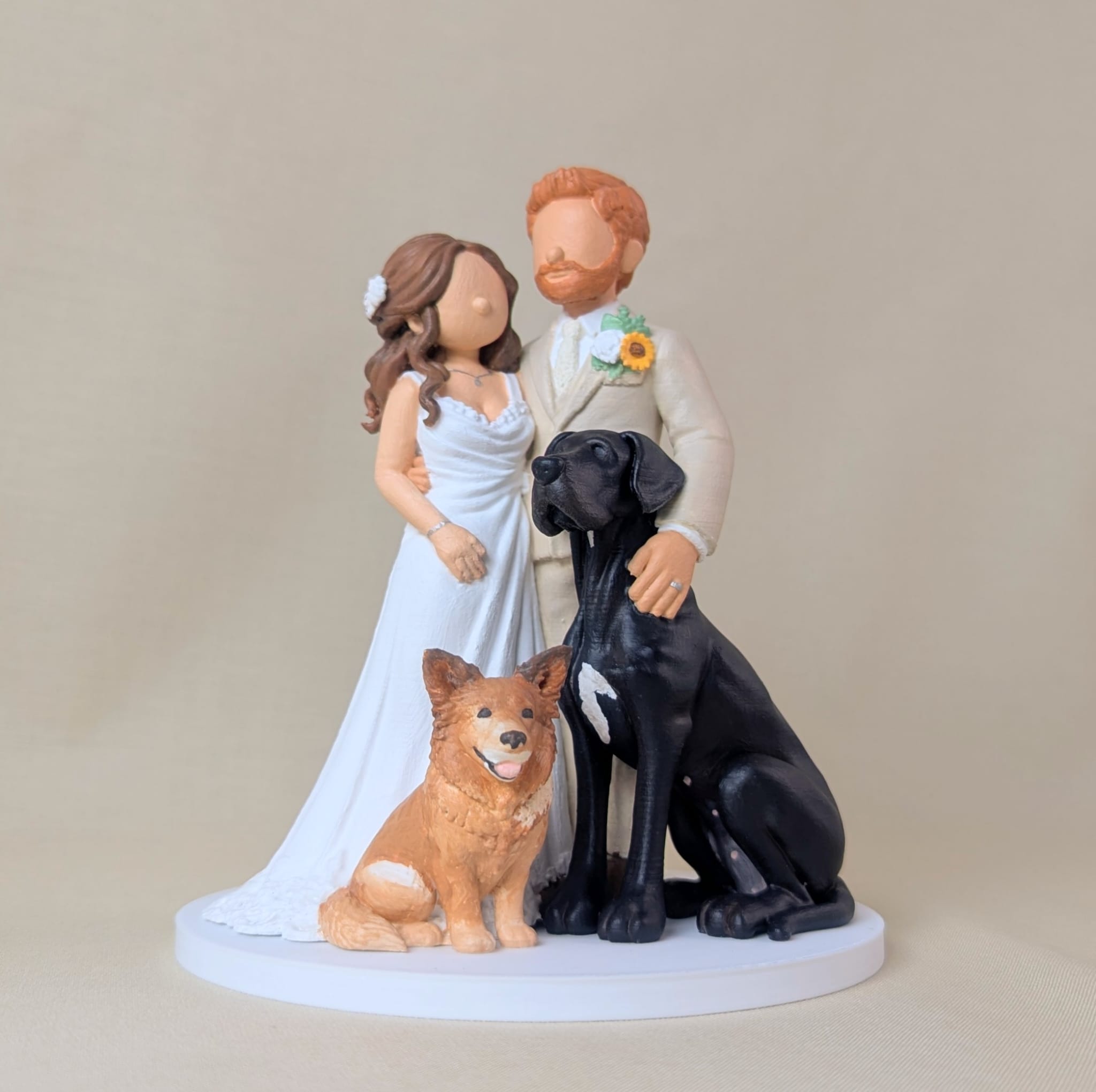 Custom wedding cake topper of a bride and groom with their two dogs, a ginger collie and a black Great Dane, the groom in a cream suit with a sunflower boutonniere